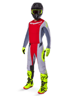Zawodnik motocrossowy w koszulce Alpinestars 2025 Techstar Melt, jaskrawoczerwona z szarymi rękawami i neonowymi żółtymi akcentami, w komplecie z dopasowanymi spodniami, jaskrawożółtymi butami i rękawicami oraz czarnym kaskiem z goglami w żółtych oprawkach, kompletny zestaw off-road.