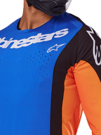 Alpinestars 2025 Techstar Melt Jersey, koszulka motocrossowa, niebieska i pomarańczowa z czarnymi panelami, białe logo Alpinestars, widoczne laserowo wycinane perforacje na klatce piersiowej, noszona przez motocyklistę w czarnym kasku
