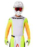 Alpinestars 2025 Techstar Melt Jersey, odzież do wyścigów motocrossowych, biały przód z neonowo-żółtymi i pomarańczowymi rękawami, zawodnik w białym kasku i czerwonych goglach, neonowo-żółte rękawice z czarnym logo, wyrazista kolorystyka dla wydajności off-road