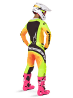 Motocrossista widoczny od tyłu w koszulce Alpinestars 2025 Techstar Melt, jaskrawy żółto-pomarańczowy gradient z czarnymi elementami, pasujące spodnie motocrossowe, jaskraworóżowe buty i biały kask, sportowy krój do rywalizacji off-road.