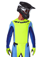 Koszulka Techstar Melt 2025, koszulka motocrossowa, żółta fluo i niebieska, z laserowo wycinaną wentylacją i sportowym krojem wyścigowym, zawodnik w czarnym kasku i żółtych rękawicach fluo
