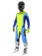 Zawodnik motocrossowy ubrany w koszulkę Alpinestars 2025 Techstar Melt, żółty neonowy i niebieski, w zestawie z pasującymi spodniami, czarnym kaskiem z goglami, żółtymi rękawicami oraz biało-czarnymi butami, kompletny i dopasowany profesjonalny ubiór do wyścigów terenowych