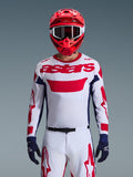 Zawodnik motocrossowy w koszulce Alpinestars 2026 Racer Riway w kolorystyce biało-niebiesko-czerwonej, duże czerwone logo „astars” na piersi, granatowe panele boczne, dopasowane biało-czerwone spodnie, czerwony kask z białymi goglami i granatowe rękawice, kompletny zestaw wyścigowy off-road