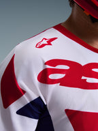 Zbliżenie na koszulkę Alpinestars 2026 Racer Riway, koszulka motocrossowa biało-niebiesko-czerwona, oddychająca, odprowadzająca wilgoć tekstura siatki, czerwone logo gwiazdy na ramieniu i wyraziste czerwone grafiki na piersi