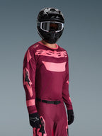 Motocyklista motocrossowy ubrany w zestaw Alpinestars 2026 Racer Riway, bordowo-różowa koszulka z wyraźnym brandingiem „astars”, pasujące spodnie z różowymi akcentami, czarny kask i rękawice, profesjonalny strój wyścigowy do motocrossu off-road
