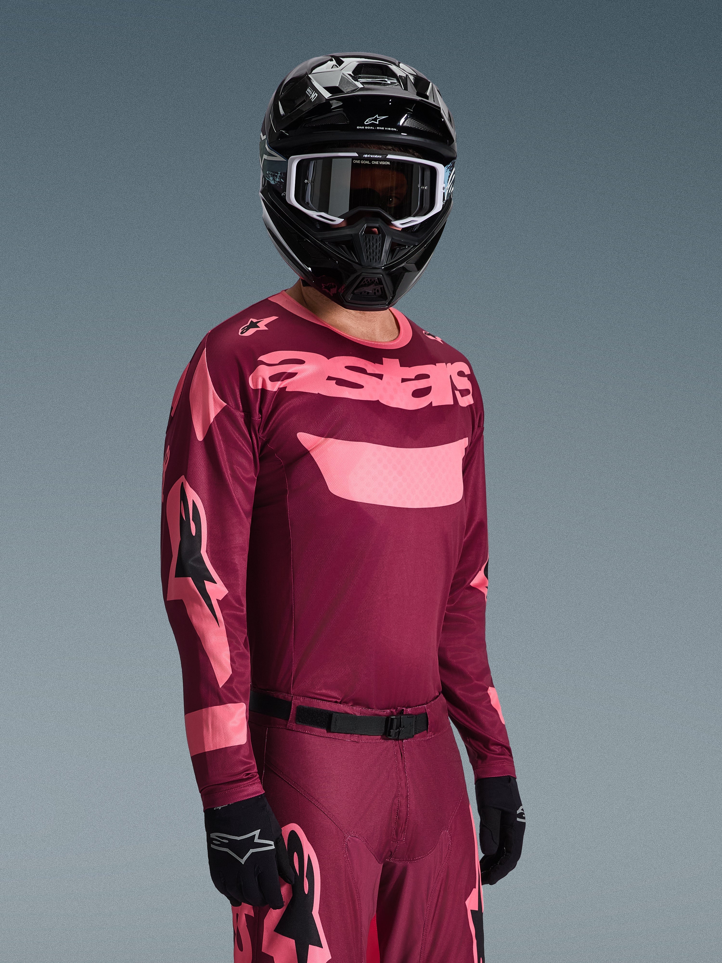 Motocyklista motocrossowy ubrany w zestaw Alpinestars 2026 Racer Riway, bordowo-różowa koszulka z wyraźnym brandingiem „astars”, pasujące spodnie z różowymi akcentami, czarny kask i rękawice, profesjonalny strój wyścigowy do motocrossu off-road