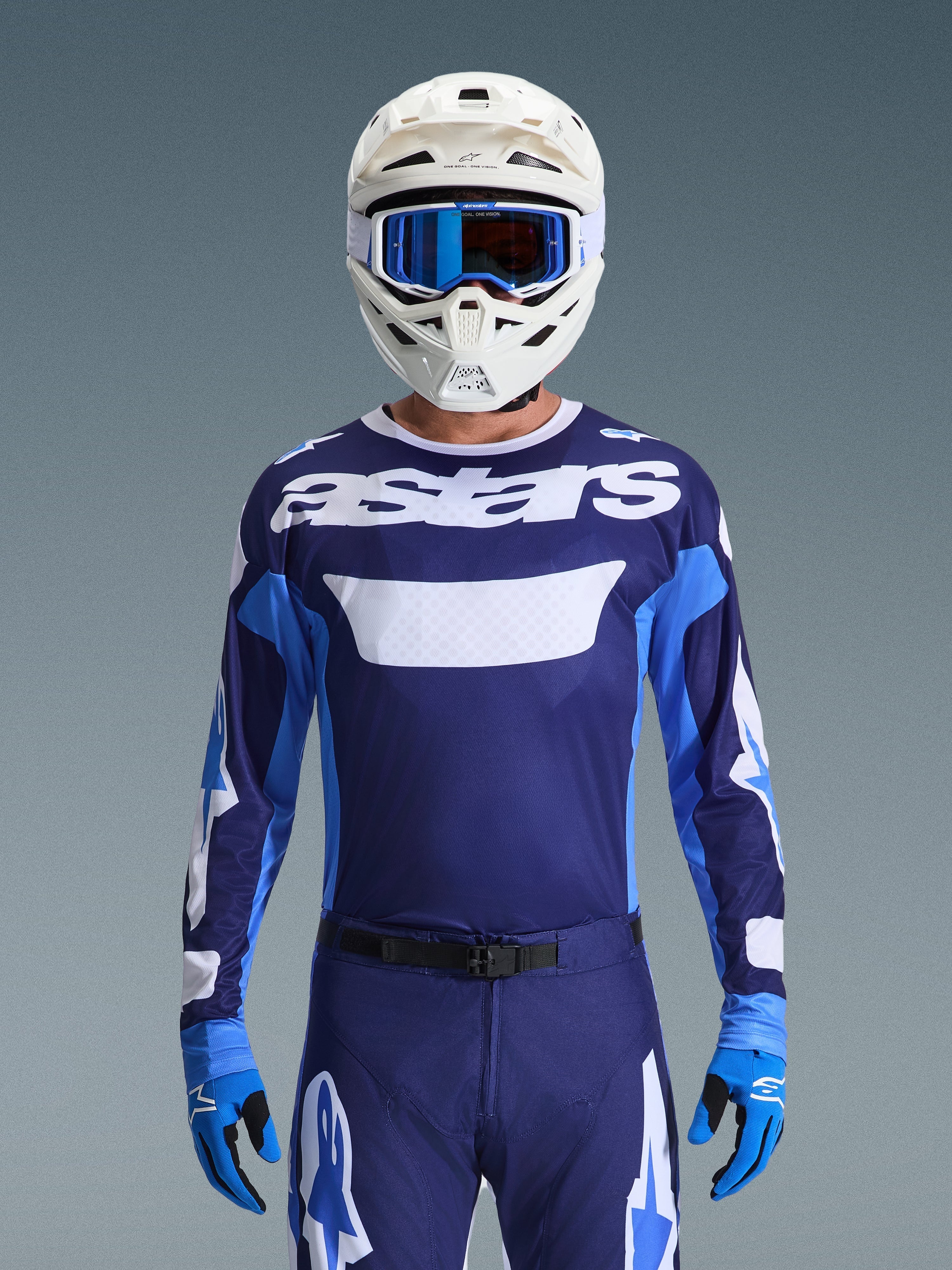 Motocyklista motocrossowy w koszulce Alpinestars 2026 Racer Riway, kolor UCLA Blue i biały z białym logo „astars” na piersi, biały kask z niebieskimi goglami, pasujące spodnie motocrossowe i niebieskie rękawice, skoordynowany zestaw odzieży off-road
