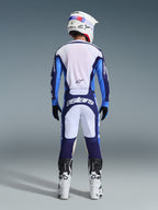 Zawodnik motocrossowy widziany od tyłu w koszulce Alpinestars 2026 Racer Riway w kolorze Ucla Blue i białym, pasujące spodnie motocrossowe z białymi i granatowymi panelami oraz logo Astars, biało-czarne buty i biały kask, kompletny, dopasowany strój wyścigowy do jazdy w terenie.