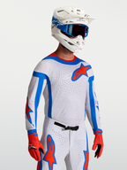 Alpinestars Koszulka Supertech Vesta, biała koszulka motocrossowa z czerwonymi i niebieskimi akcentami, elastyczna siatka o sportowym kroju, profesjonalna odzież wyścigowa MX na modelu.