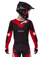 Alpinestars 2025 Racer Veil Jersey, koszulka motocrossowa, czarno-jaskrawoczerwona, noszona z dopasowanymi spodniami, czarnym kaskiem i czerwonymi goglami, wyraziste białe logo i nowoczesny wyścigowy design, profesjonalna odzież do motocrossu terenowego