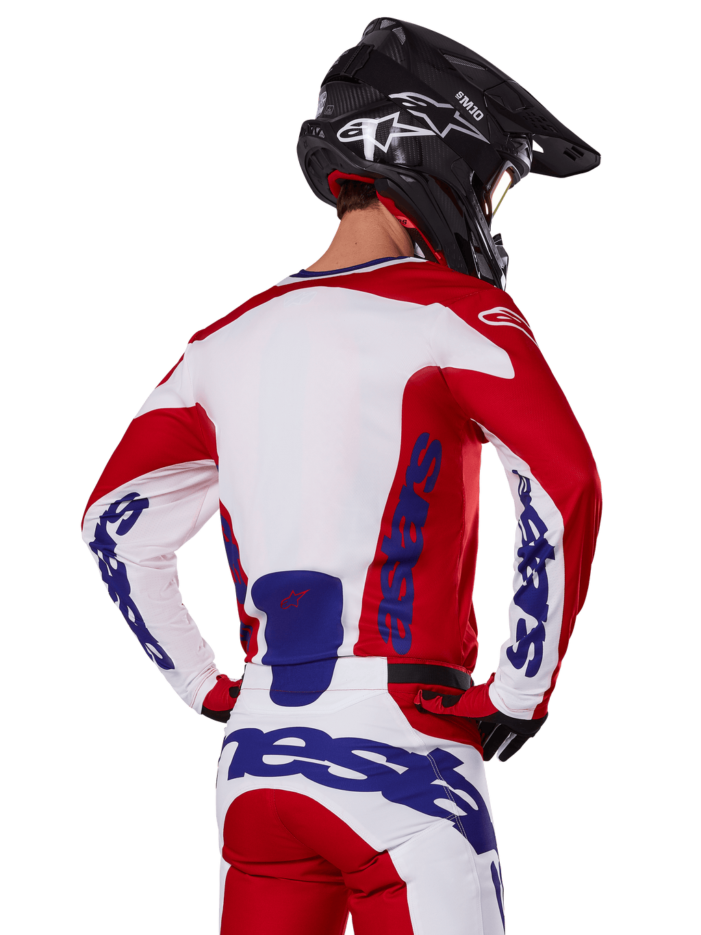 Alpinestars 2025 Racer Veil Jersey and Pants, zestaw odzieży motocrossowej, jaskrawoczerwony, biały i niebieski, widok z tyłu motocyklisty w pasującym zestawie i czarnym kasku motocrossowym, wyraźne niebieskie logo Alpinestars, techniczna odzież wyścigowa off-road