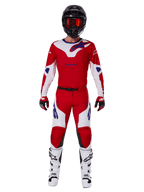 Zawodnik motocrossowy w zestawie Alpinestars 2025 Racer Veil, jaskrawoczerwona i biała koszulka oraz spodnie z niebieskimi akcentami, czarny kask z czerwonymi goglami, białe buty i czerwono-czarne rękawice, profesjonalny strój do jazdy terenowej