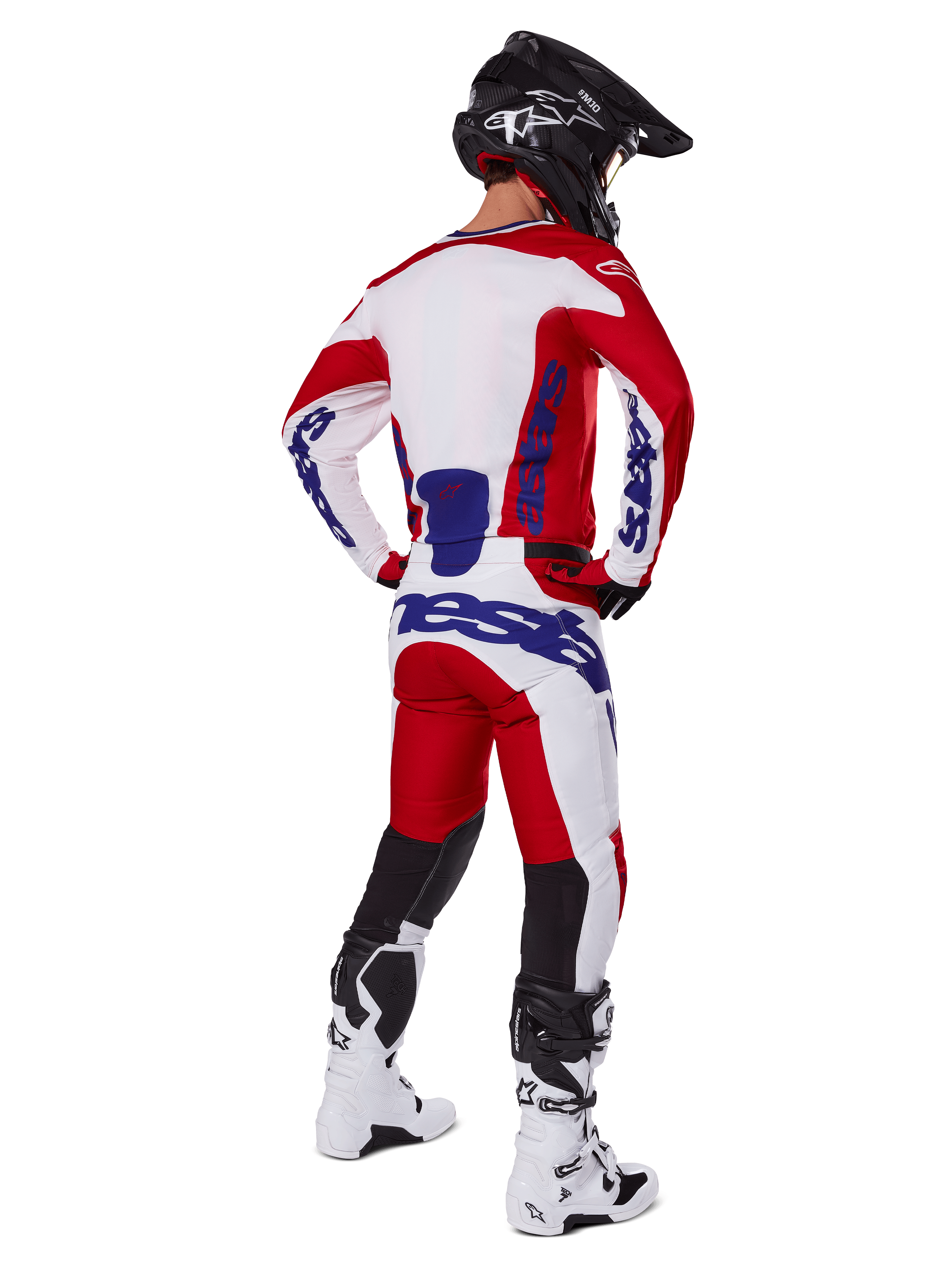 Motocyklista motocrossowy widoczny od tyłu, ubrany w koszulkę i spodnie Alpinestars 2025 Racer Veil w kolorze czerwonym i białym, niebieski branding, czarny kask i białe buty, kompletny zestaw odzieży do wyścigów terenowych