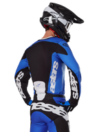 Alpinestars 2025 Racer Veil Gear Set, strój motocrossowy, niebiesko-czarno-biały, widok z tyłu motocyklisty w koszulce i spodniach z wyraźnym brandingiem, czarno-biały kask, dopasowany zestaw do jazdy off-road