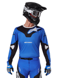 Koszulka 2025 Racer Veil, koszulka motocrossowa, niebieska i czarna, noszona z dopasowanym sprzętem motocrossowym, w tym kaskiem i rękawicami, sportowy design z białym brandingiem Alpinestars
