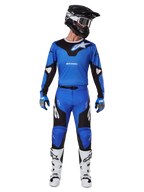 Motocyklista motocrossowy w zestawie Alpinestars 2025 Racer Veil, niebiesko-czarna koszulka i dopasowane spodnie, czarny kask z białymi goglami, biało-czarne buty, skoordynowany strój wyścigowy do jazdy terenowej motocross.