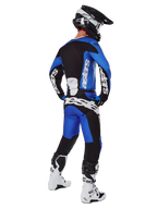 Motocyklista motocrossowy w pełnym stroju wyścigowym widziany od tyłu, koszulka Racer Veil 2025 i pasujące spodnie w kolorze niebieskim i czarnym, z białym brandingiem Alpinestars, czarny kask, biało-czarne buty, skoordynowany zestaw do wyścigów terenowych
