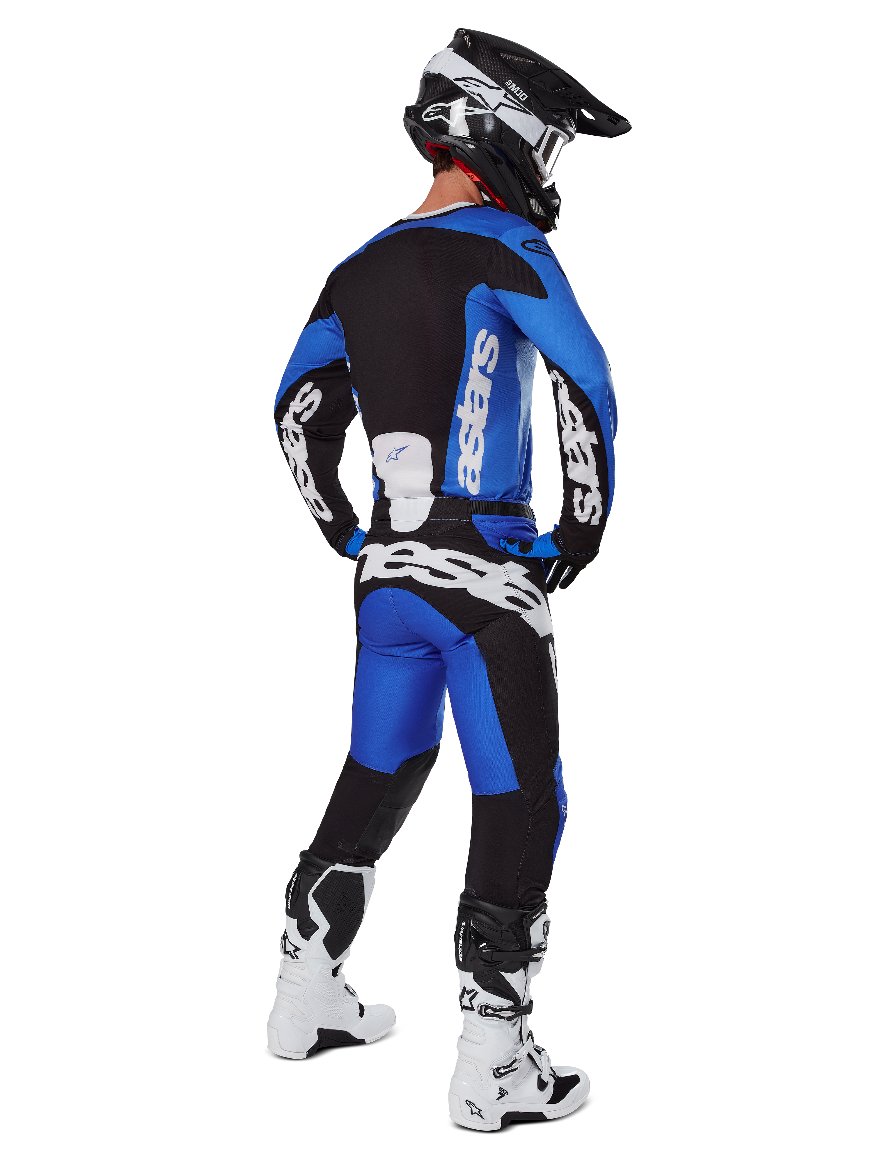 Motocyklista motocrossowy w pełnym stroju wyścigowym widziany od tyłu, koszulka Racer Veil 2025 i pasujące spodnie w kolorze niebieskim i czarnym, z białym brandingiem Alpinestars, czarny kask, biało-czarne buty, skoordynowany zestaw do wyścigów terenowych