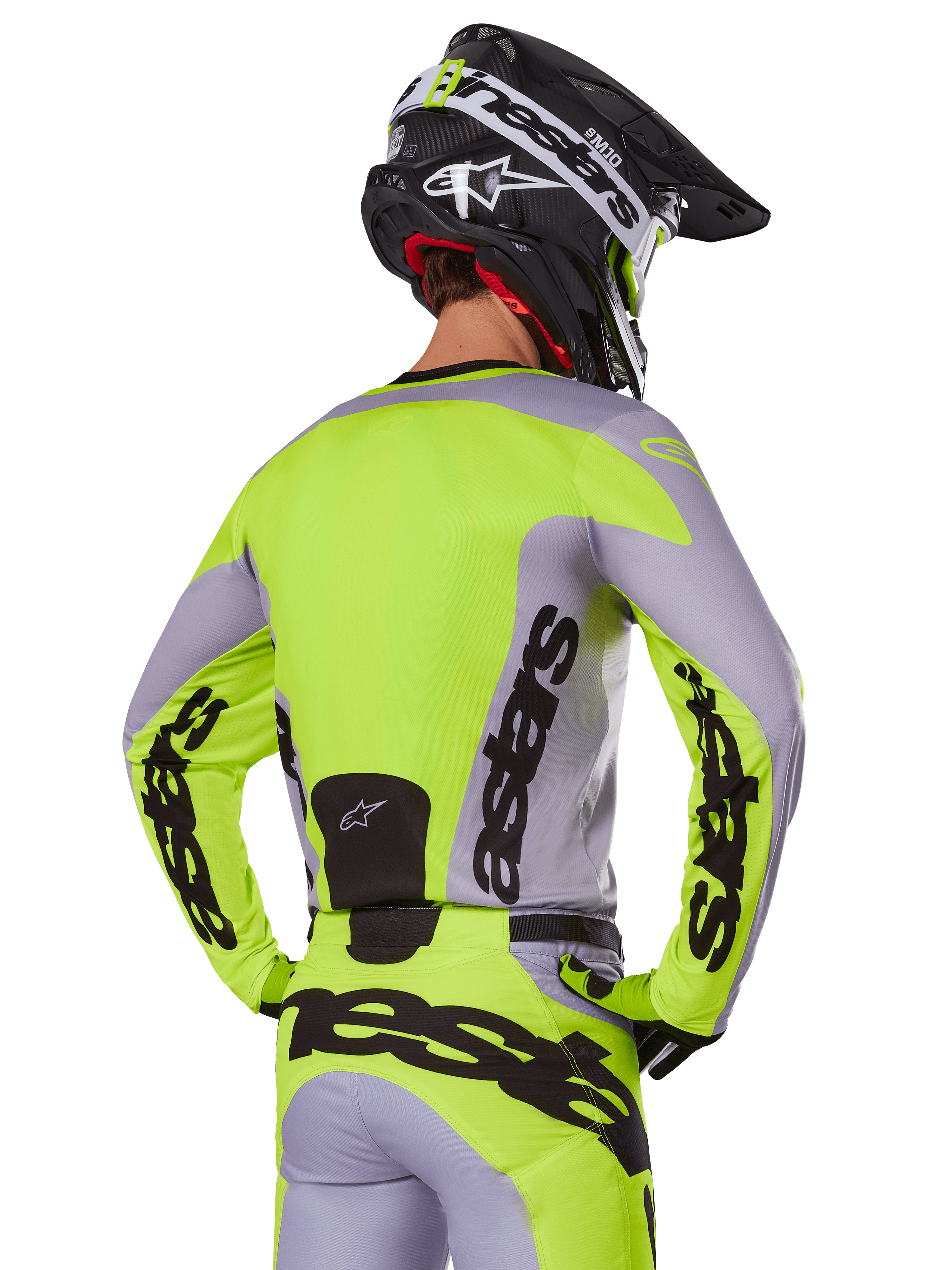 Zawodnik motocrossowy od tyłu w koszulce Alpinestars 2025 Racer Veil w kolorze szarym i neonowym żółtym, z wyraźnym logo „astars” na plecach i rękawach, w zestawie z dopasowanymi spodniami i czarnym kaskiem, kompletny strój wyścigowy