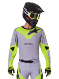 Alpinestars Racer Veil Jersey 2025, koszulka motocrossowa, szara i neonowo-żółta, fason z długim rękawem z czarnym logo Alpinestars, pokazana jako część kompletnego stroju wyścigowego z dopasowanymi spodniami, czarnym kaskiem i rękawicami