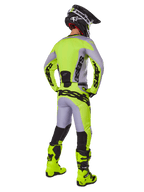 Motocyklista motocrossowy widoczny od tyłu w zestawie Alpinestars 2025 Racer Veil, szaro-neonowożółta koszulka i spodnie, dopasowane neonowożółte buty oraz czarno-żółty kask, skoordynowany strój do wyścigów terenowych