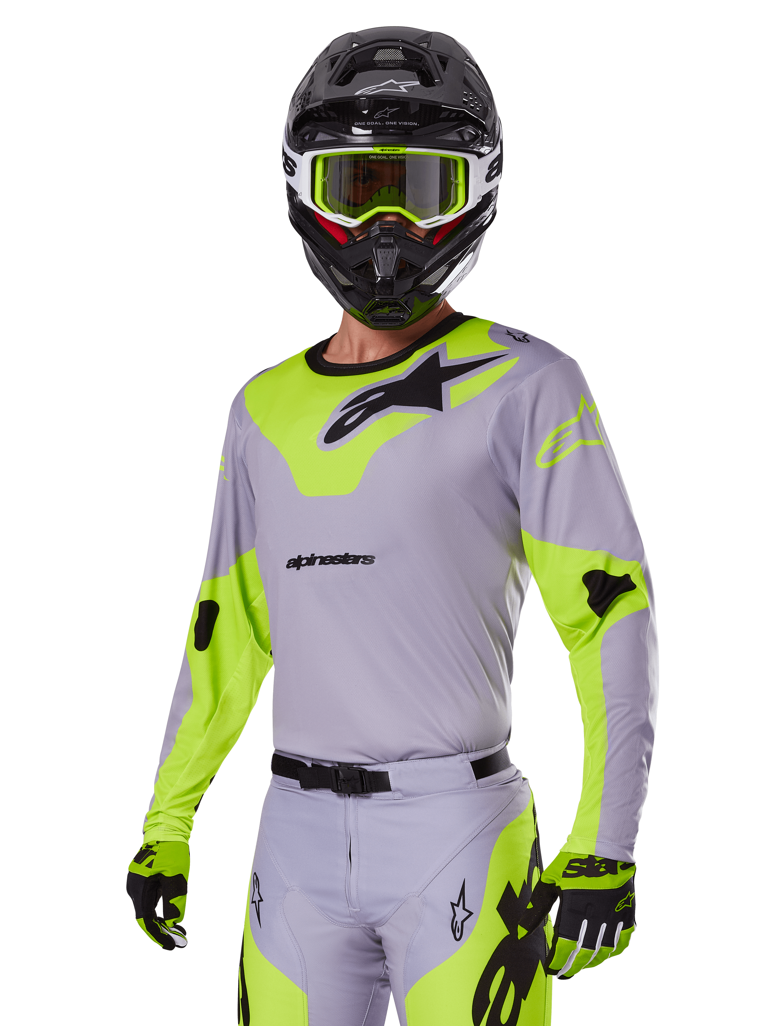 Zawodnik motocrossowy w zestawie Alpinestars 2025 Racer Veil w kolorze szarym i neonowym zielonym, jasnoszara koszulka i spodnie z wyrazistymi neonowymi żółto-zielonymi panelami i czarnym logo Alpinestars, dopasowane rękawice i czarny kask z neonowymi zielonymi goglami, profesjonalna odzież wyścigowa off-road.