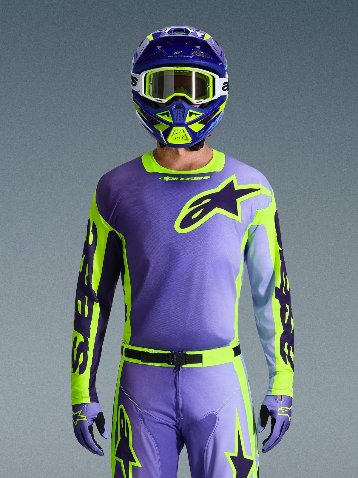 Koszulka Alpinestars 2026 Racer Portl, koszulka motocrossowa, fioletowa i żółta fluo, noszona z dopasowanymi spodniami motocrossowymi, rękawicami i kaskiem, z dużym logo gwiazdy Alpinestars na piersi, zdjęcie studyjne na szarym tle