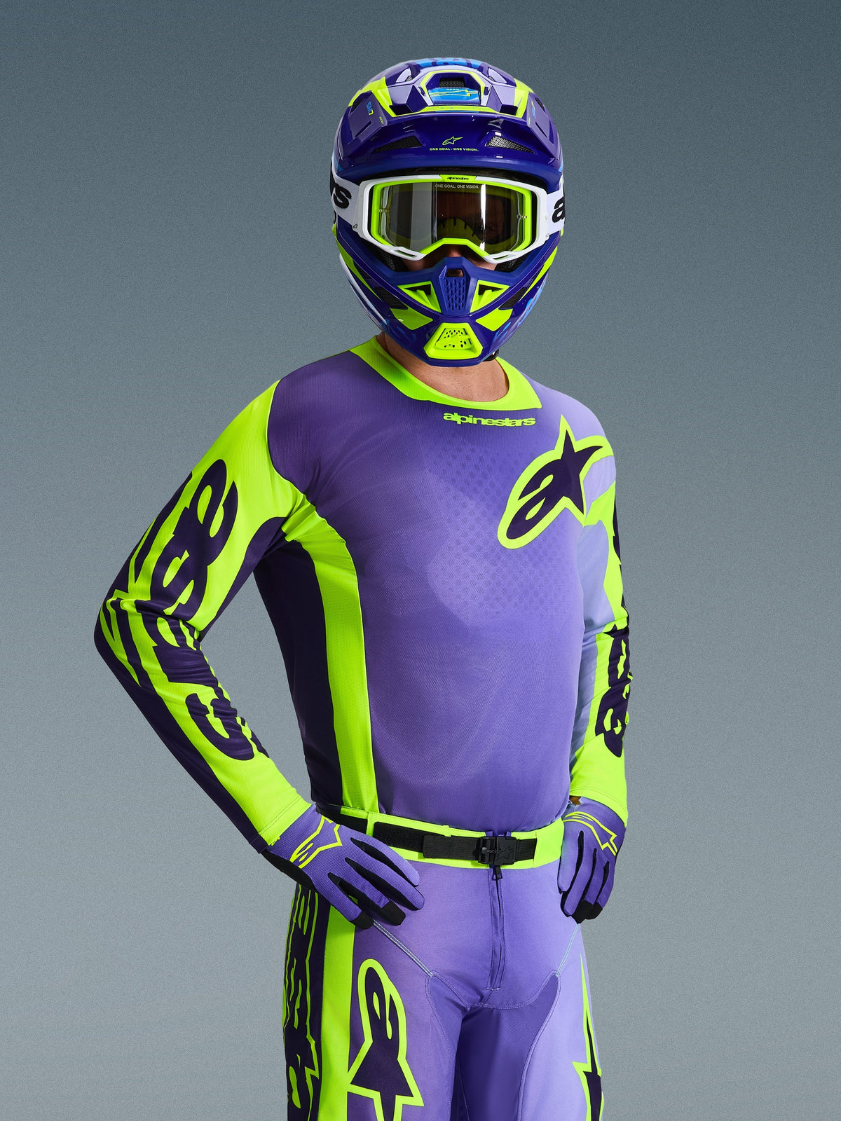Kierowca motocrossowy w koszulce Racer Portl 2026, fioletowy i żółty neonowy, dopasowany fioletowo-żółty kask z białymi goglami, fioletowo-żółte rękawice, kompletny zestaw odzieży do jazdy off-road