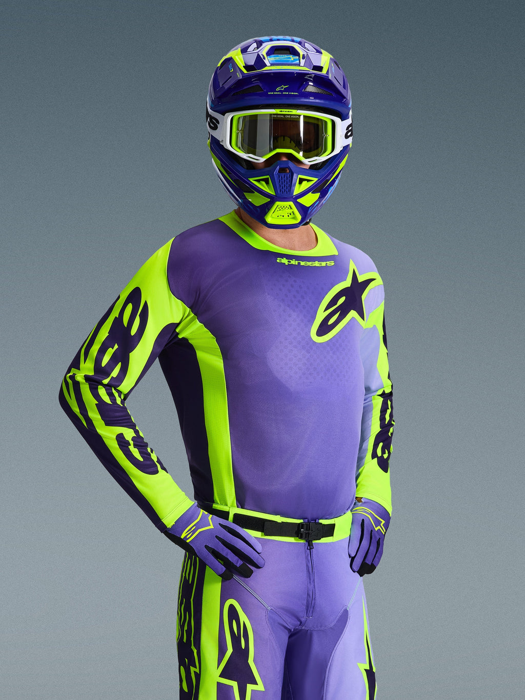 Kierowca motocrossowy w koszulce Racer Portl 2026, fioletowy i żółty neonowy, dopasowany fioletowo-żółty kask z białymi goglami, fioletowo-żółte rękawice, kompletny zestaw odzieży do jazdy off-road