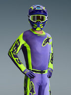 Kierowca motocrossowy w koszulce Racer Portl 2026, fioletowy i żółty neonowy, dopasowany fioletowo-żółty kask z białymi goglami, fioletowo-żółte rękawice, kompletny zestaw odzieży do jazdy off-road