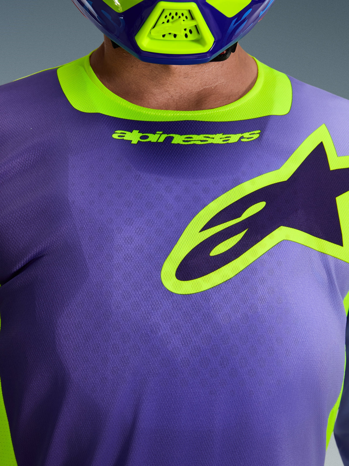 Alpinestars 2026 Racer Portl Jersey, koszulka motocrossowa, fioletowa i żółta fluo, zbliżenie na klatkę piersiową z dużym logo Alpinestars z żółtym obrysem, elastyczny kołnierzyk z brandingiem, techniczny poliester odprowadzający wilgoć