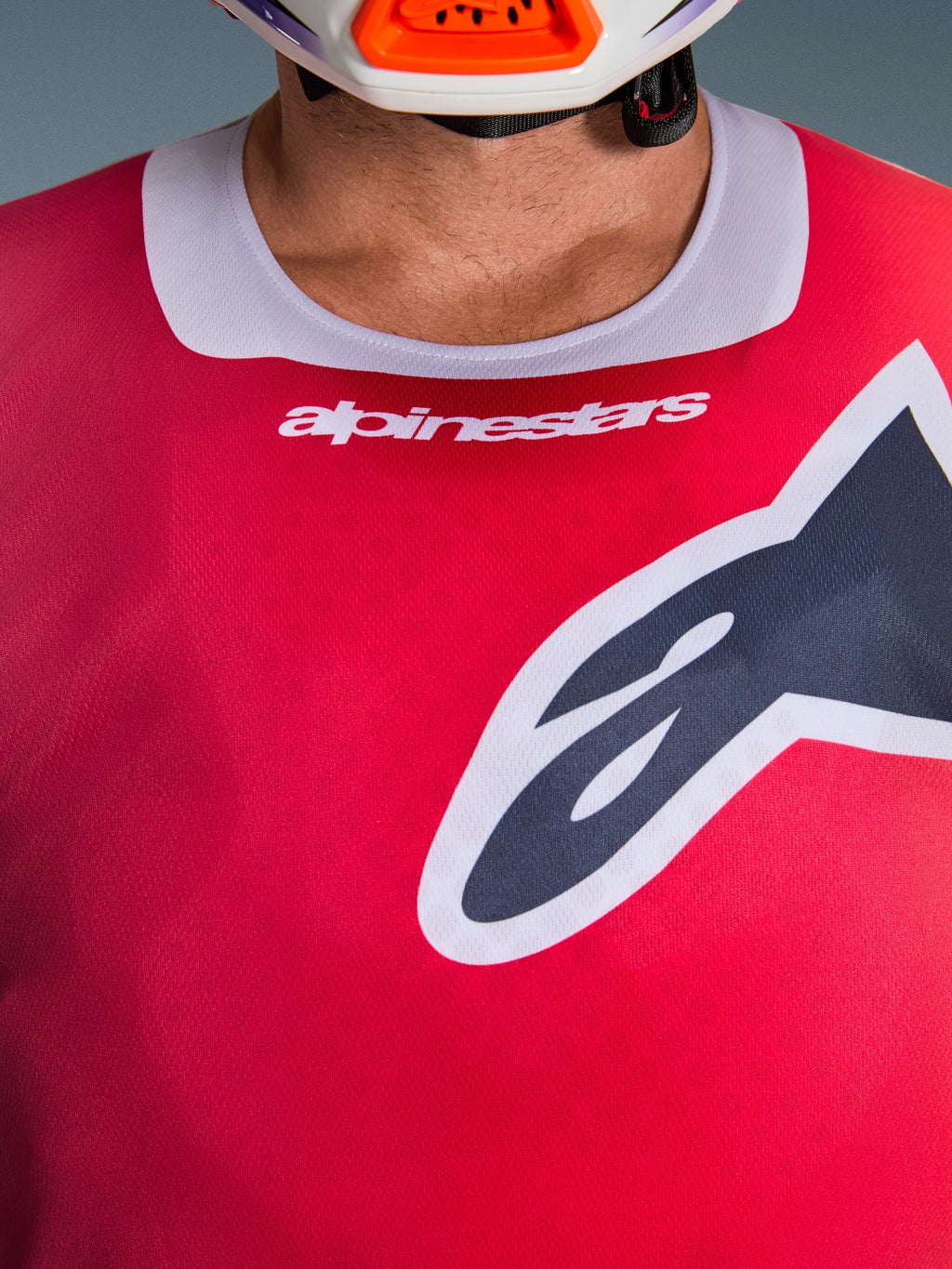 Alpinestars 2026 Racer Portl Jersey, zbliżenie na klatkę piersiową i kołnierzyk, kolor czerwony z jasnoszarym wykończeniem, biały napis Alpinestars i duże logo Astars, widoczna tekstura technicznego materiału odprowadzającego wilgoć