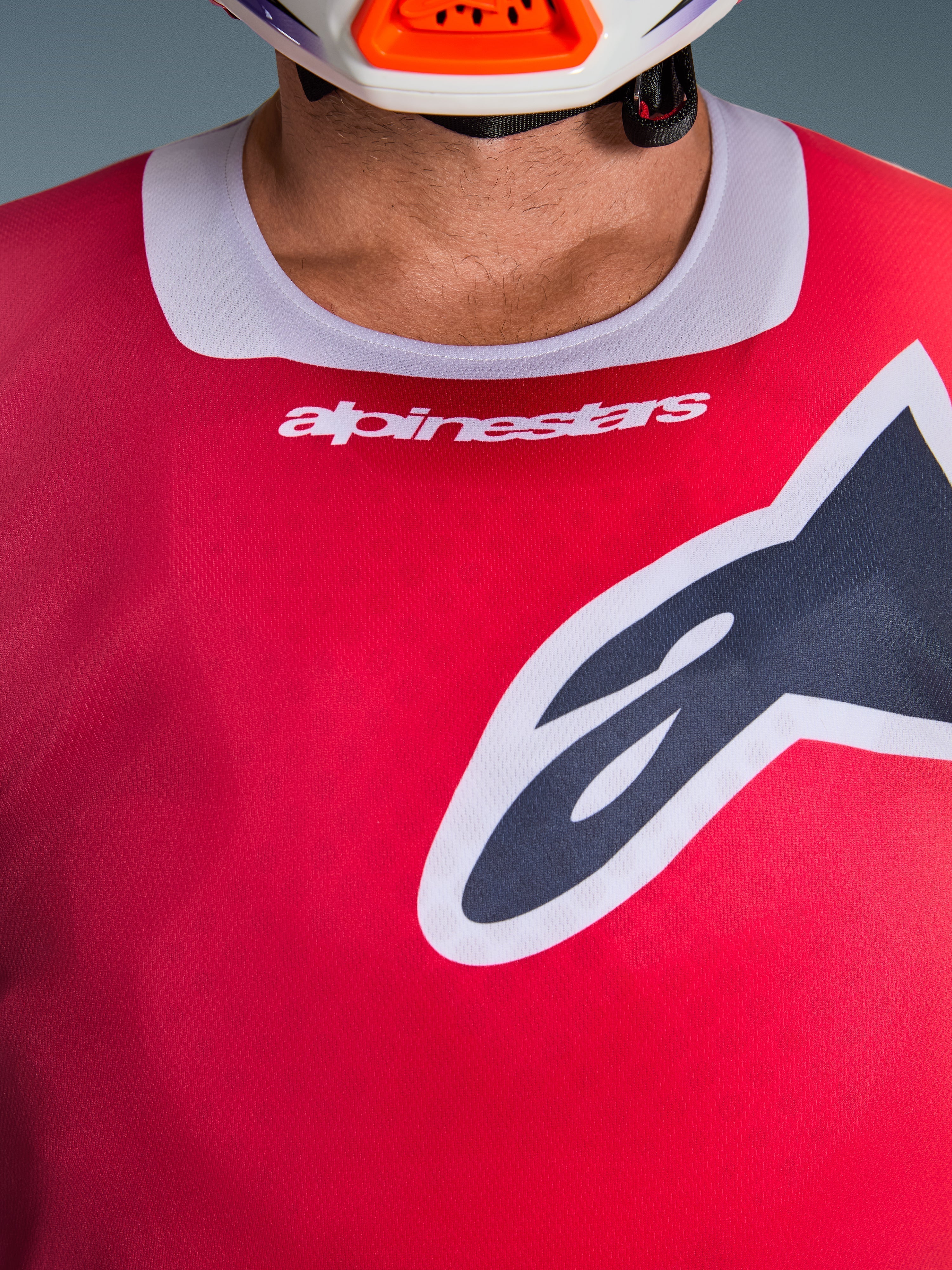 Zbliżenie na koszulkę Alpinestars 2026 Racer Portl w kolorze czerwonym, z jasnoszarym elastycznym kołnierzykiem z białym logo i dużym czarnym logo Astars na piersi, wyczynowa odzież do motocrossu