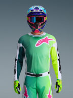 Zestaw Alpinestars 2026 Racer Portl, zawodnik motocrossowy w koszulce z zielono-żółtym gradientem i różowym logo Astars, pasujące spodnie, kolorowy niebiesko-różowy kask z niebieskimi goglami i limonkowe rękawice, profesjonalny strój wyścigowy off-road