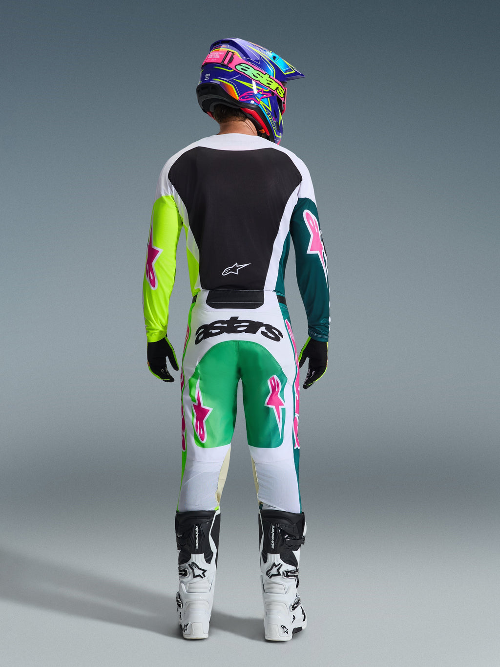 Zawodnik motocrossowy widziany od tyłu, ubrany w koszulkę 2026 Racer Portl Jersey w kolorze zielono-biało-czarnym, z czarnym panelem na plecach i asymetrycznymi zielonymi rękawami z różowymi logo gwiazdy, w stylizacji z dopasowanymi spodniami motocrossowymi i białymi butami.
