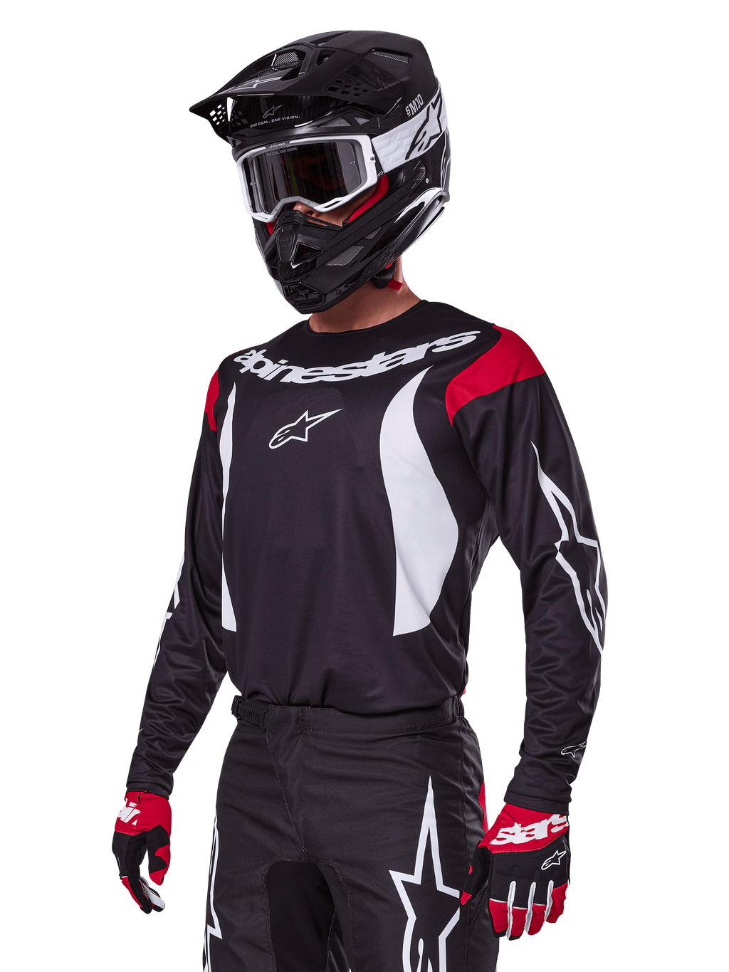 Motocyklista motocrossowy ubrany w zestaw Alpinestars 2025 Fluid Haul, czarna koszulka z czerwonymi panelami na ramionach i białą grafiką, pasujące czarne spodnie z białym logo gwiazdy, czerwono-czarne rękawice, czarny kask z białymi akcentami i gogle, dopasowana odzież motocrossowa.