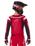 Alpinestars 2025 Fluid Haul Jersey, koszulka motocrossowa, jaskrawoczerwona i czarna, noszona jako część kompletnego zestawu z pasującymi spodniami i rękawicami, czarny kask z goglami z żółtymi szybkami, białe logo i branding, wysokiej klasy odzież do wyścigów off-road