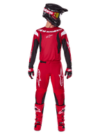 Zestaw Alpinestars 2025 Fluid Haul, strój motocrossowy w kolorze jasnoczerwonym i czarnym, czerwona koszulka z czarnymi rękawami i białym brandingiem, pasujące czerwone spodnie z białym logo gwiazdy, czarny kask ze złotymi goglami i czerwone buty, kompletny sprzęt do jazdy terenowej