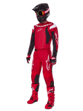 Zawodnik motocrossowy ubrany w zestaw Alpinestars Fluid Haul 2025, jasnoczerwony z czarnymi i białymi akcentami, kompletny strój zawierający koszulkę, spodnie, kask, buty i rękawice, zaprojektowany dla wydajności i ochrony off-road