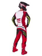 Motocyklista motocrossowy od tyłu w zestawie Alpinestars 2025 Fluid Haul, jaskrawoczerwony i czarny z białymi panelami, neonowożółte logo na rękawach i spodniach, dopasowane czerwone buty i czarny kask, kompletny profesjonalny strój do jazdy terenowej