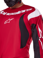 Koszulka Alpinestars 2025 Fluid Haul, jasnoczerwona i czarna, zbliżenie na klatkę piersiową i ramię z białym logo i brandingiem Alpinestars, sportowy ergonomiczny design, czarne i białe dynamiczne akcenty, odzież do motocrossu.
