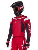 Zawodnik motocrossowy w zestawie Alpinestars 2025 Fluid Haul w kolorze czerwonym, czerwona koszulka z białymi i czarnymi akcentami, pasujące czerwone spodnie z białą grafiką, czarny kask z białym logo, czerwono-żółte gogle, czerwono-czarne rękawice, kompletny strój wyścigowy do motocrossu