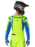 Alpinestars 2025 Fluid Haul Jersey, koszulka motocrossowa, neonowy żółty i niebieski, z niebieskim logo Alpinestars na klatce piersiowej, noszona z dopasowanym sprzętem, w tym czarnym kaskiem i niebieskimi rękawicami, sportowy krój do jazdy off-road