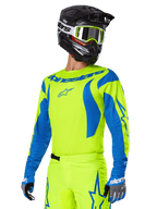 Alpinestars 2025 Fluid Haul Gear Set, koszulka i spodnie motocrossowe, jaskrawożółty i niebieski, czarny kask i gogle w żółtych oprawkach, niebieskie wzory przypominające fale na rękawach i niebieskie logo gwiazdy na spodniach, dopasowany strój do wyścigów terenowych