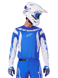 Alpinestars 2025 Fluid Haul Jersey, koszulka motocrossowa, niebiesko-biała, noszona z pasującymi spodniami i rękawicami, biały kask z niebieskimi goglami, dopasowany zestaw odzieży MX do jazdy terenowej