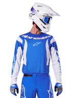 Alpinestars 2025 Fluid Haul Jersey, koszulka motocrossowa, niebiesko-biała, noszona z pasującymi spodniami i rękawicami, biały kask z niebieskimi goglami, dopasowany zestaw odzieży MX do jazdy terenowej