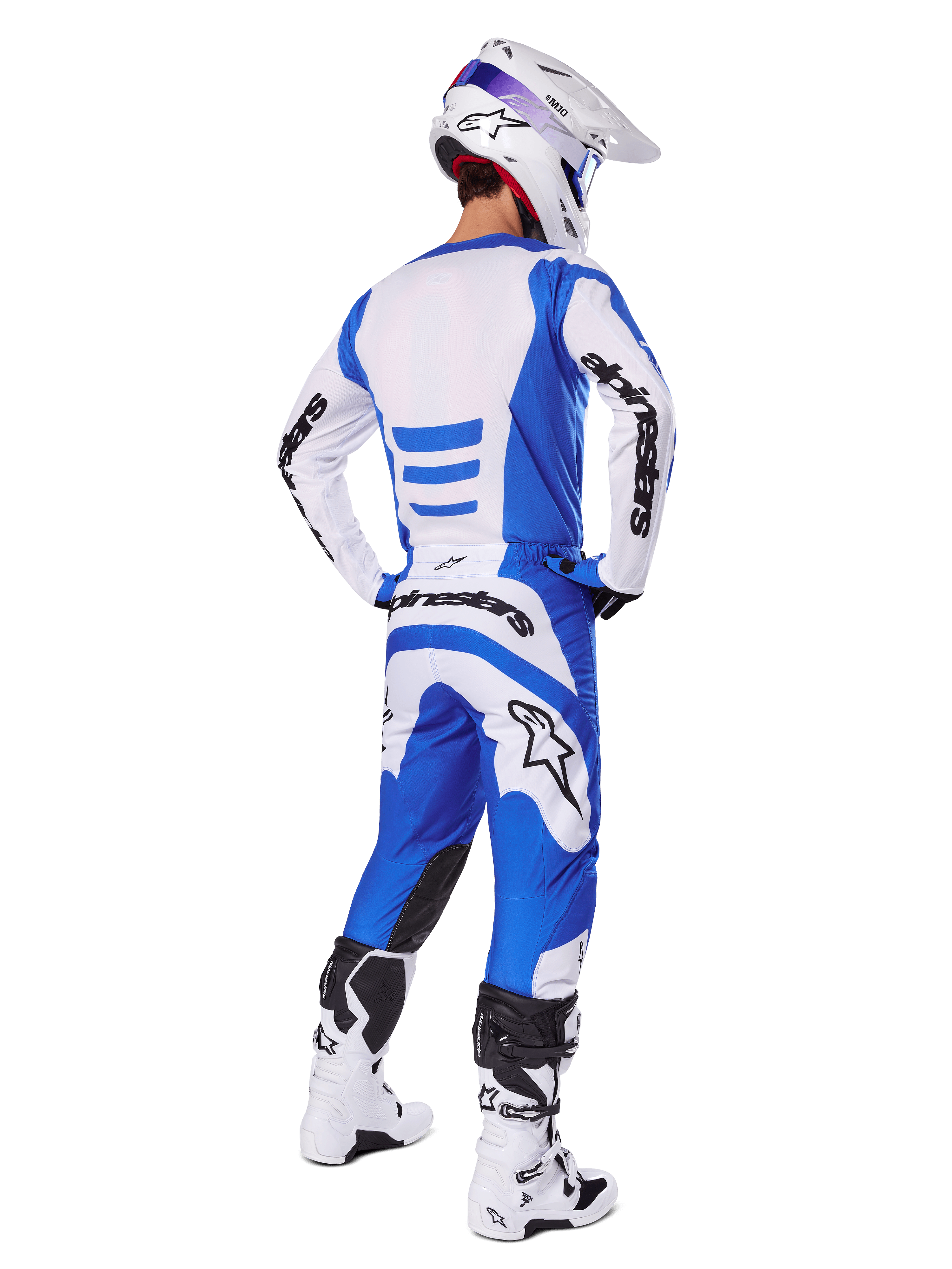 Jeździec motocrossowy widziany od tyłu w zestawie Alpinestars 2025 Fluid Haul, niebiesko-biała koszulka i pasujące spodnie, biały kask z niebieskimi akcentami oraz biało-czarne buty wyścigowe, dopasowany strój do jazdy terenowej