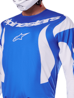 Alpinestars 2025 Fluid Haul Jersey, niebiesko-biała koszulka motocrossowa noszona przez zawodnika w białym kasku, biały napis Alpinestars i logo A-star, sportowy krój, lekki materiał odprowadzający wilgoć, do motocrossu i jazdy terenowej