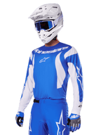 Zawodnik motocrossowy w zestawie Alpinestars 2025 Fluid Haul w kolorze niebiesko-białym, niebieska koszulka z białymi akcentami, pasujące niebieskie spodnie z logo gwiazdy, biały kask z niebieskimi goglami i dopasowane niebiesko-szare rękawice, kompletny strój wyścigowy off-road