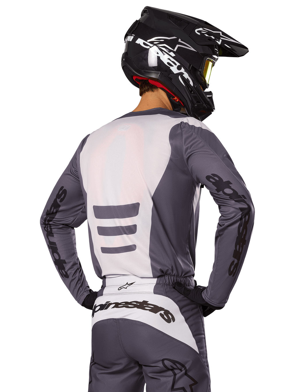 Zawodnik motocrossowy od tyłu w zestawie Alpinestars 2025 Fluid Haul, szaro-biała koszulka i spodnie, czarny kask z białą grafiką, żółte gogle, dopasowany strój wyścigowy